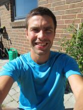 Greg Nowak sitting and smiling in a blue t-shirt.